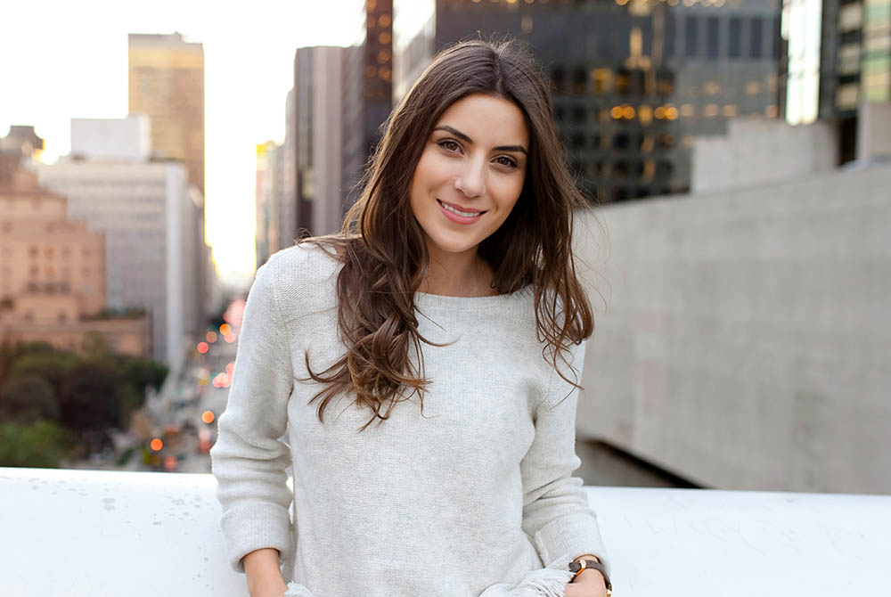 Beautiful young woman sitting on a bridge across the boulevard in urban scenery, downtown, at sunset, smilin-1000x670
