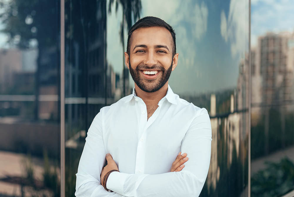 Portrait of a young confident smiling indian man with his arms crossed looking into the camera-1000x670-1000x670