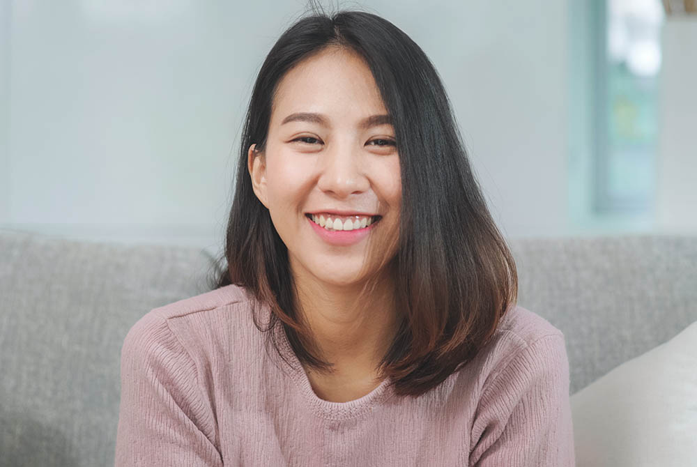 Teenager Asian woman feeling happy smiling and looking to camera while relax in living room at home. Lifesty-1000x670
